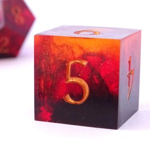 May include: A set of red and gold dice with black numbers. The dice are made of resin and have a marbled effect. One die is showing the number 5.