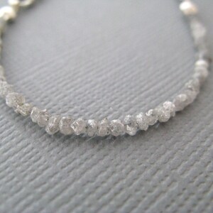 Puede incluir: Un brazalete delicado hecho con una hebra de peque&ntilde;os diamantes blancos en bruto. Los diamantes est&aacute;n enhebrados en una cadena de plata.