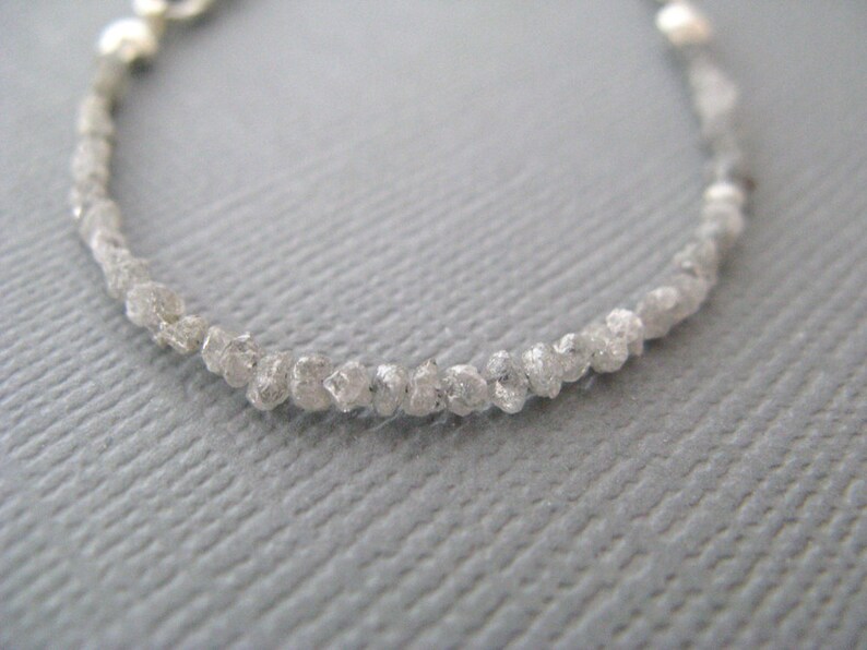 Puede incluir: Un brazalete delicado hecho con una hebra de peque&ntilde;os diamantes blancos en bruto. Los diamantes est&aacute;n enhebrados en una cadena de plata.