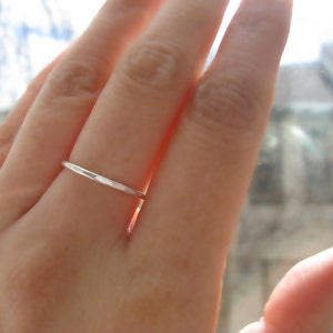 Puede incluir: Primer plano de una mano con un anillo de banda de plata delgada.