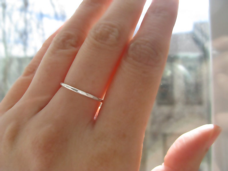 Puede incluir: Primer plano de una mano con un anillo de banda de plata delgada.