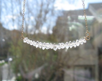 Puede incluir: Un delicado collar de cadena dorada con una fila de cuentas de cristal transparentes y facetadas.