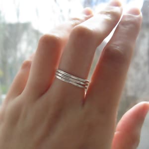 Puede incluir: Primer plano de una mano con tres anillos apilables de plata. Los anillos son finos y tienen una textura martillada.