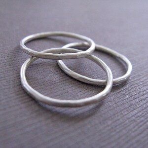 Puede incluir: Tres anillos de plata apilados uno encima del otro. Los anillos son todos lisos y tienen una textura martillada.