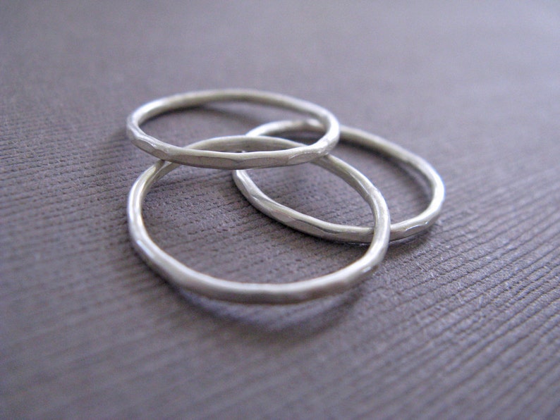 Puede incluir: Tres anillos de plata apilados uno encima del otro. Los anillos son todos lisos y tienen una textura martillada.