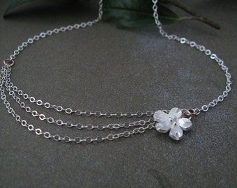 Puede incluir: Un delicado collar de plata con tres hilos y un pequeño y detallado colgante de flores. El collar presenta una fina cadena y está acentuado con un toque de oro rosa. El colgante de flores mide aproximadamente 1,3 cm de diámetro.