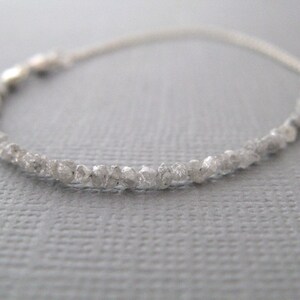 Puede incluir: Un delicado brazalete de cadena de plata con una fila de peque&ntilde;os diamantes blancos en bruto.