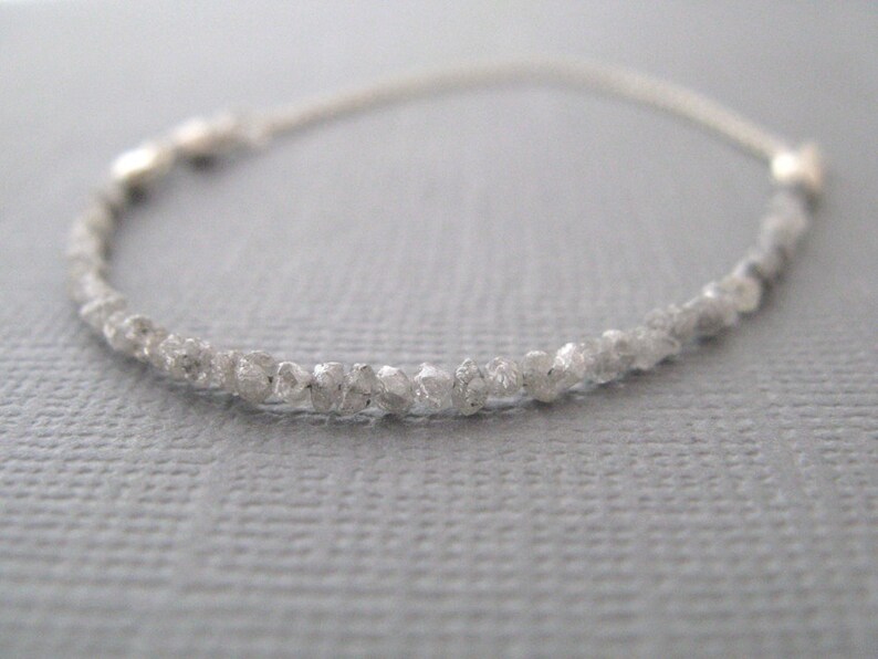 Puede incluir: Un delicado brazalete de cadena de plata con una fila de peque&ntilde;os diamantes blancos en bruto.