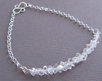 Puede incluir: Un brazalete de cadena de plata con un acento de cristal transparente. Los cristales son facetados y tienen un aspecto áspero y natural.
