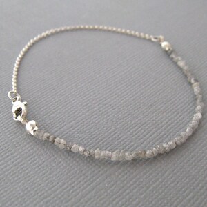 Puede incluir: Un brazalete de cadena de plata con un cierre de plata y una hebra de peque&ntilde;os diamantes grises en bruto.