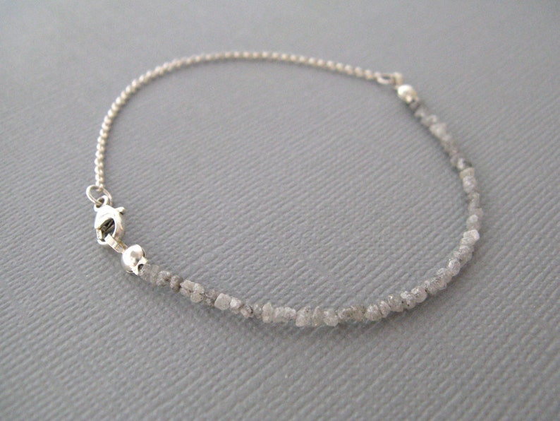Puede incluir: Un brazalete de cadena de plata con un cierre de plata y una hebra de peque&ntilde;os diamantes grises en bruto.