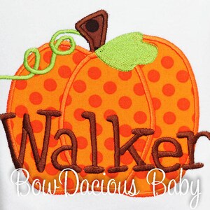 May include: Embroidered orange pumpkin with brown polka dots, green stem, and the name "Walker" in brown thread. The text "Bow Dacious Baby" is below the pumpkin. The design is on a white background.