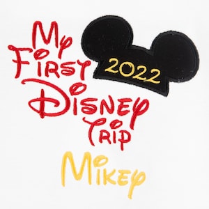 May include: White t-shirt with red embroidered text that says "My First Disney Trip" and "Mickey" in yellow. A black Mickey Mouse head with a yellow hat that says "2022" is above the text.