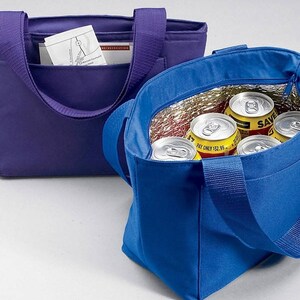 K&ouml;nnte beinhalten: Zwei isolierte Lunch-Taschen, eine lila und eine blaue. Die blaue Tasche ist offen und enth&auml;lt mehrere Dosen Limonade. Die Taschen haben einen Rei&szlig;verschluss und einen oberen Griff.