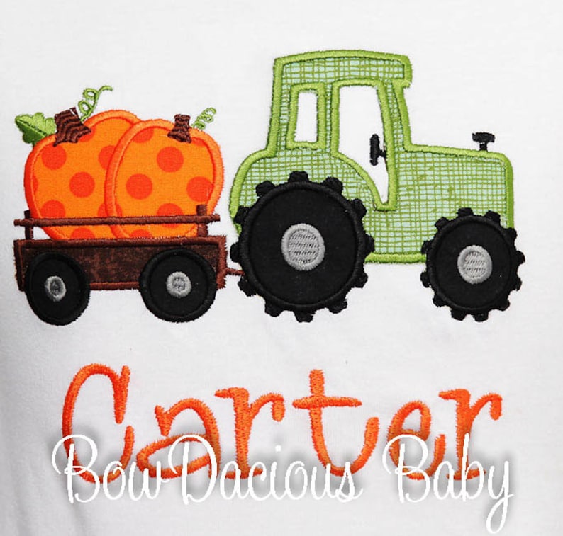 May include: White shirt with an embroidered design featuring a green tractor pulling a wagon filled with two orange pumpkins. The name "Carter" is embroidered in orange script, with "Bow Dacious Baby" below.