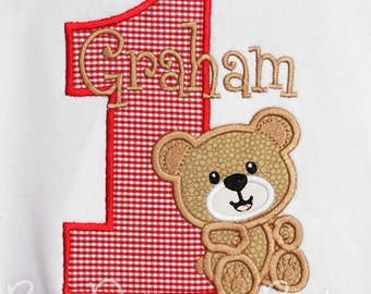 May include: Red and white gingham number one with the name Graham embroidered in brown. A brown teddy bear is sitting to the right of the number one. The text "Bow Dacious Baby" is at the bottom of the image.