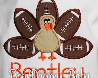 May include: White t-shirt featuring a Thanksgiving turkey design. The turkey's feathers are footballs, and the design includes the name "Bentley" in orange script, with the text "Bow Dacious Baby" below.