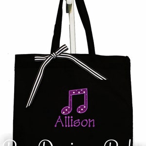 May include: Black canvas tote bag with a white and black striped ribbon bow. The bag has a purple musical note with white polka dots and the name "Allison" embroidered on it. The text "Bow Dacious Baby" is printed on the bottom of the bag.