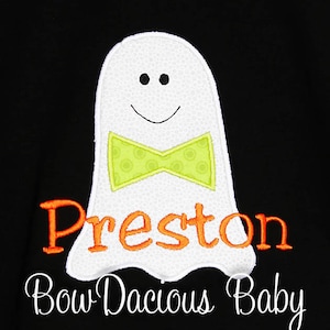 May include: White ghost applique with a green bow tie and the name "Preston" in orange lettering. The text "Bow Dacious Baby" is written in cursive below the ghost on a black background.