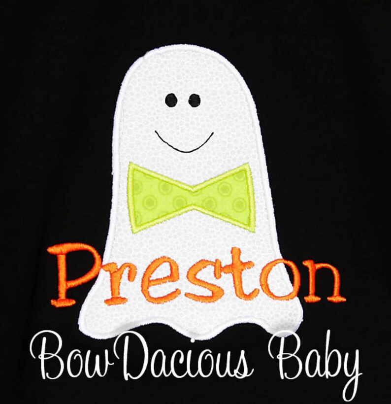 May include: White ghost applique with a green bow tie and the name "Preston" in orange lettering. The text "Bow Dacious Baby" is written in cursive below the ghost on a black background.