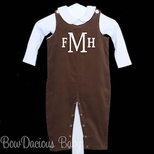May include: Brown corduroy baby romper with white long-sleeve shirt underneath. The romper features a white monogram with the letters F, M, and H. The outfit has a Peter Pan collar and button closures.