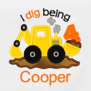 May include: A yellow toy excavator with a brown dirt mound and the text "I dig being 4" in orange and black. The name "Cooper" is written in orange below the excavator.