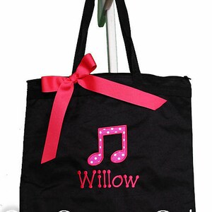 May include: Black canvas tote bag with a pink polka dot musical note and the name "Willow" embroidered on the front. The bag has a pink satin ribbon bow.