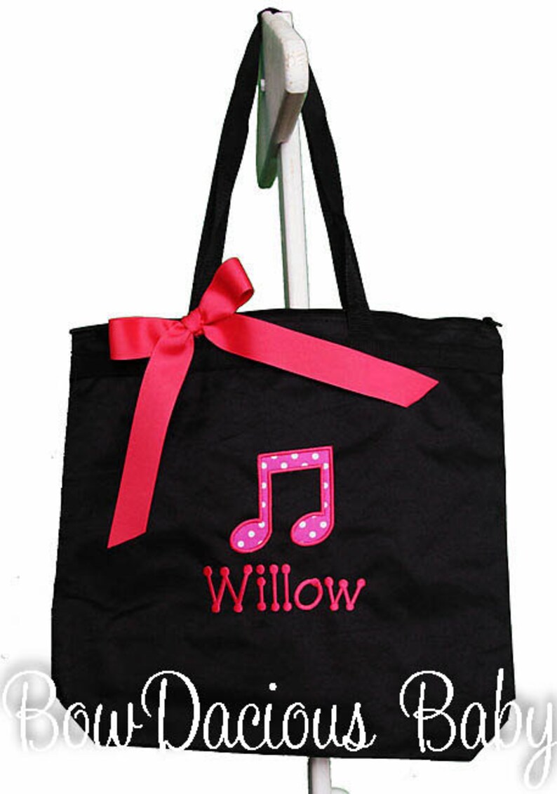 May include: Black canvas tote bag with a pink polka dot musical note and the name "Willow" embroidered on the front. The bag has a pink satin ribbon bow.