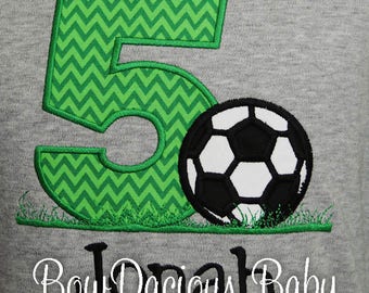 May include: Green and white chevron number five with a black and white soccer ball on a gray background. The text "Bow Dacious Baby" is below the number and soccer ball.