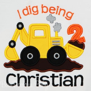 May include: A yellow toy construction vehicle with a brown dirt pile and the number 2 in orange. The text "I dig being" is above the vehicle and the name "Christian" is below the vehicle.
