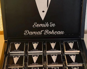 May include: A black box with a tuxedo design on the lid. The box is open and contains 16 small black and white chocolate squares with the text "Semih'in Damat Bohcasi" on each square.