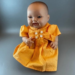 May include: A yellow dress with white buttons and a white collar on a baby doll.