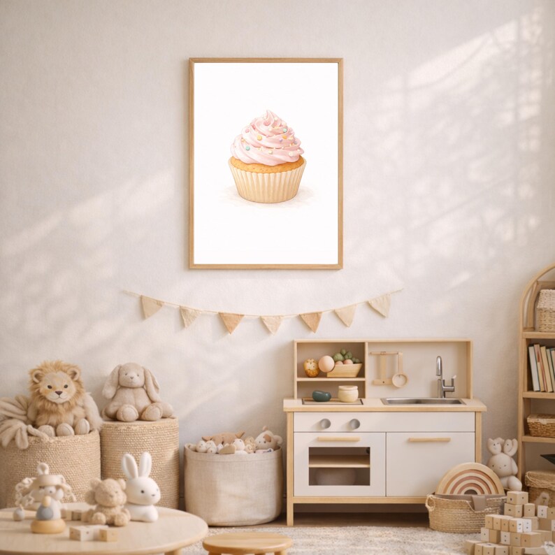 May include: A framed watercolor print of a cupcake with pink frosting and sprinkles. The cupcake is in a tan paper cup. The print is in a light brown wooden frame. The image is hanging on a white wall in a child's playroom.