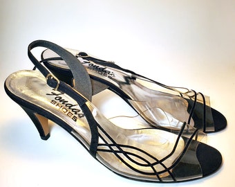May include: Black suede heeled sandals with a clear plastic strap design and "Jondar's Shoes" printed on the side.