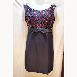 May include: A sleeveless black dress with a burgundy and black sequined bodice and a black satin bow at the waist.