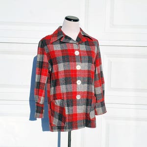 Puede incluir: Una chaqueta de cuadros rojos y grises con cierre de botones y un bolsillo de parche en el lado izquierdo.