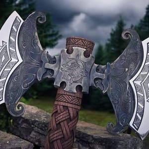 May include: A double-bladed axe with intricate carvings. The axe features a silver-colored head with detailed patterns and a wooden handle with a woven design. The blades have a white edge. The background shows a forest and cloudy sky.