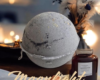 May include: A large, round, gray bath bomb with gold flecks and a textured surface. A dark glass jar with a label sits next to the bath bomb. The word "Moonlight" is written in cursive at the bottom.