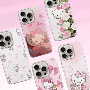May include: A collection of pink and white phone cases featuring Hello Kitty designs. The cases showcase various illustrations, including bows, roses, and the iconic character with a teddy bear. The cases are designed to fit a smartphone with a multi-lens camera.