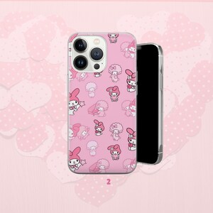 Puede incluir: Funda de tel&eacute;fono rosa con un patr&oacute;n repetido de personajes de dibujos animados. La funda tiene un borde transparente y se ve un tel&eacute;fono negro detr&aacute;s. El fondo es rosa claro con formas de coraz&oacute;n.
