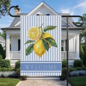 Puede incluir: Una bandera de jardín con una ilustración de acuarela de limones y hojas verdes sobre un fondo de rayas azules y blancas. La palabra "WELCOME" se muestra en letras blancas en una pancarta azul en la parte inferior.