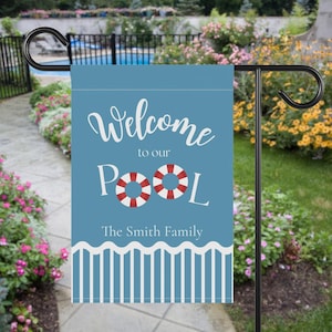 May include: A blue garden flag with the words "Welcome to our Pool" in white script, featuring two red and white life preservers. The flag also includes "The Smith Family" and a white and blue border design.