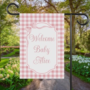 May include: A pink and white gingham garden flag with the text "Welcome Baby Alice" in elegant script. The flag features a decorative bow and is designed for outdoor use, perfect for welcoming a new baby.