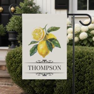 May include: A cream-colored garden flag featuring a watercolor illustration of lemons with green leaves. The name "THOMPSON" is printed in black, centered below the lemon illustration, with decorative flourishes above and below.