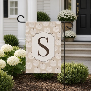 May include: A rectangular garden flag featuring a light tan background with a repeating pattern of white line-art pumpkins. In the center, a white decorative frame contains a large, dark brown capital letter S in a serif font.