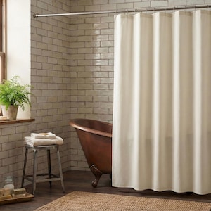 May include: A bathroom scene featuring a cream-colored shower curtain, a copper bathtub, and a small stool with towels. A window with a potted plant and a brick wall complete the rustic aesthetic. The room has a natural, spa-like feel.