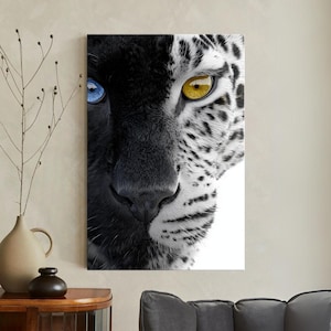 Może przedstawiać: Wydruk na płótnie przedstawiający podzielony obraz twarzy jaguara. Jedna strona to czarna pantera z niebieskim okiem, druga to biały jaguar z żółtym okiem. Grafika prezentuje uderzający kontrast kolorów i faktur.