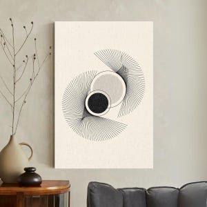 May include: Abstract art print featuring a geometric design with two overlapping circles, one black and one light gray, set against a cream-colored background. Thin black lines radiate from the circles, creating a fan-like pattern.