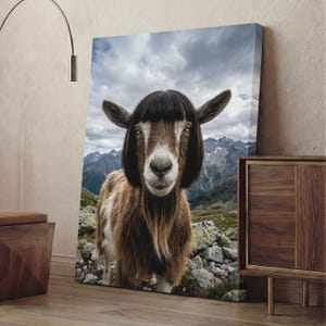 May include: A canvas print featuring a goat with a black wig, set against a backdrop of mountains and a cloudy sky. The goat has brown and white fur and is looking directly at the viewer. The print is displayed on a wooden floor.