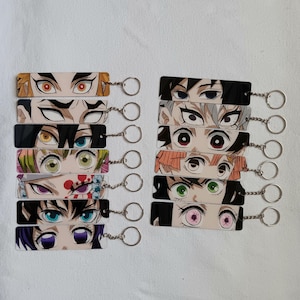 May include: A collection of rectangular keyrings, each showcasing anime-style eye designs. The keyrings feature diverse eye styles and colours, attached to silver keyrings. The keyrings are arranged in two columns against a white backdrop.